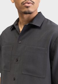 Kurzärmliges graues Hemd aus glattem Stoff, mit zwei Vorderentaschen und klassischem Kragen.