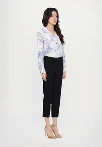 Langermet bluse med blå blomsterprint på bakgrunn av kremfarge, kombinert med svarte smale bukser og nude stroppede høye hæler.