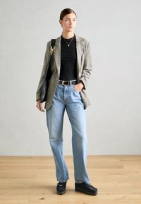 Plaid švarkas rusvai juodai, juoda palaidinė, šviesiai mėlyni aukštu juosmeniu džinsai ir juodi platforminiai batai, su juoda petine rankine.