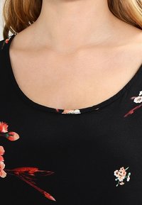 Top negro con un escote amplio que presenta un patrón floral en rojo y blanco, fabricado con una tela suave de textura agradable.