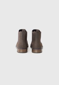 Botas de cuero marrón hasta el tobillo con paneles laterales elásticos, punta redondeada y una entresuela de madera. Cuenta con una lengüeta en la parte trasera para ponérselas fácilmente.
