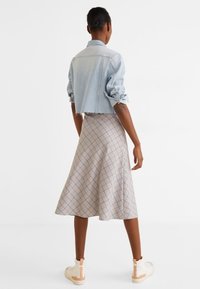 Veste courte en denim bleu clair portée sur une jupe midi beige à carreaux. La jupe s'évase avec un motif géométrique, associée à des baskets blanches.