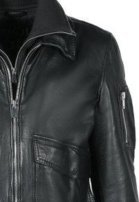 Svart läderjacka med dragkedja, ribbad krage och sidofickor. Har en ficka med dragkedja på vänster ärm och en jämn textur.