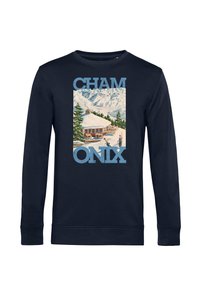 Camisa de manga larga azul marino con una cabaña en la montaña nevada, pinos, esquiadores y la palabra "CHAMONIX" en grandes letras azules.