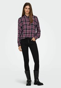 Rutig flanellskjorta i marinblått, rött och vitt; lång ärm, knäppning framtill, kombinerad med svarta tajta jeans och knähöga svarta stövlar.