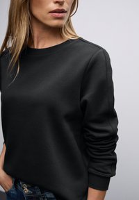 Felpa nera con collo rotondo e polsini a coste. Realizzata in tessuto morbido con una superficie liscia. Vestibilità slim con dettagli di design minimi.