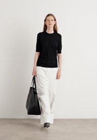 Svart strikket topp med korte ermer, kombinert med vide hvite bukser. Modellen bærer en stor svart tote-bag og har på seg svarte høyhælte sko.