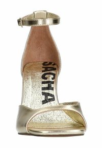 Gouden metallic hoge hak sandaal met enkelbandje, open teen ontwerp en een getextureerde inlegzool met zwart merklogo. Gladde, glanzende oppervlakte.