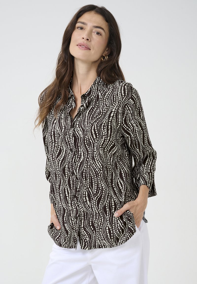 Black and white patterned blouse featuring a wave design, button-down front, and three-quarter sleeves. Soft fabric with a relaxed fit.