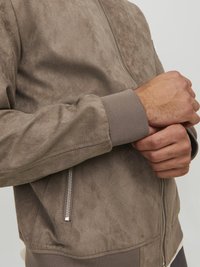 Giacca bomber in suede marrone con chiusura a zip, polsini a coste e tasca laterale, caratterizzata da una texture morbida e un design pulito.