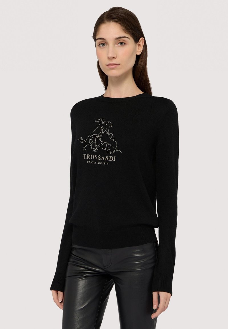 Svart stickad tröja med långa ärmar och rundad halsringning, prydd med en grå broderad grafisk design av hundar och texten "TRUSSARDI GENTLE SOCIETY."