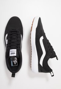 Zwarte sneakers van mesh en synthetische materialen, met witte accenten en een gestructureerde rubberen zool met een bruin loopvlak.