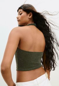 Grön metallisk halterneck crop top med en texturerad tyg, som har en åtsittande siluett och öppen ryggdesign. Slät hudton synlig.
