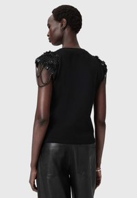 Czarny dziergany top z teksturowanymi czarnymi zdobieniami na ramionach, ozdobiony łańcuszkami. Dopasowany i bezrękawnik.