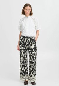 Blouse blanche avec des manches en broderie de point d'esprit, associée à un pantalon large à motif noir et blanc avec un ourlet décoratif.