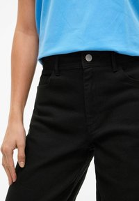 Czarne dżinsy z wysokim stanem, przednimi kieszeniami oraz metalowym guzikiem, zestawione z jasnoniebieskim bawełnianym topem.