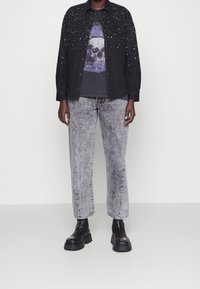 Black denim shirt with silver studs on shoulders, gray graphic T-shirt featuring a skull design, gray acid-wash straight-leg jeans, black chunky boots.