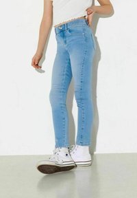 Nehybné světle modré skinny džíny vyrobené z denimu, s vysokým pasem, mají přední kapsy a zapínání na knoflík. Skombinované s bílými vysokými teniskami.
