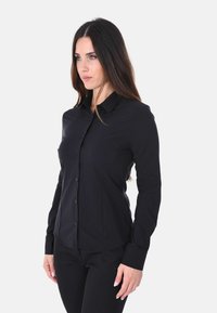 Camicia nera a maniche lunghe con bottoni, realizzata in tessuto liscio, con collo a collare, silhouette aderente e una sottile texture.