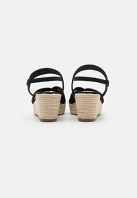 Černé espadrilky na klínu s tkanou juty, kotníkovými pásky a hladkým semišovým vzhledem, s zaobleným designem špičky.