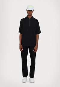 Svart kortermet polo med glidelås, med preget merkevare. Kombinert med sorte bukser og hvite sneakers. Lys blå caps med neonlys.