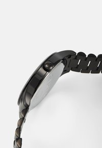 Reloj de acero inoxidable negro con una caja redonda, bisel texturizado y un diseño de pulsera de eslabones. La corona está posicionada a las 3 en punto.
