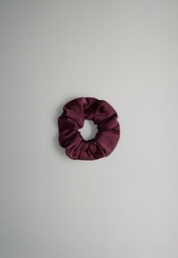 Coletero de tela color púrpura oscuro con textura suave y fruncida, centrado sobre un fondo liso de color gris claro.