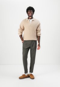 Maglione a coste beige, pantaloni grigi con motivo e scarpe marroni. Design semplice con una vestibilità comoda e materiali testurizzati.