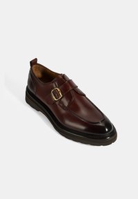 Bordeauxfarbene Lederschuhe mit glatter Oberfläche, breitem Riemen und goldener Schnalle, runder Zehenform und schwarzer Gummisohle.