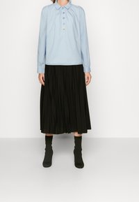 Camicia azzurra a maniche lunghe con colletto, abbinata a una gonna midi plissettata nera e stivaletti neri aderenti alla caviglia.