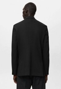 Blazer nero su misura con taglio classico, rever a punta e polsini abbottonati, realizzato in un tessuto liscio con una silhouette strutturata.