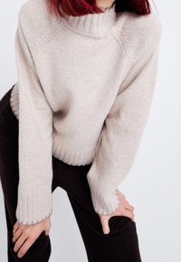 Pull tricoté beige clair avec un col montant côtelé, des poignets et un ourlet côtelés. Texture douce, coupe ajustée et silhouette décontractée.