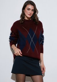 Bordo in mornarjska barva v argyle vzorcu pulover s sproščenim krojem, rebrastimi manšetami in okroglo ovratnikom, v kombinaciji s temnim krilom.