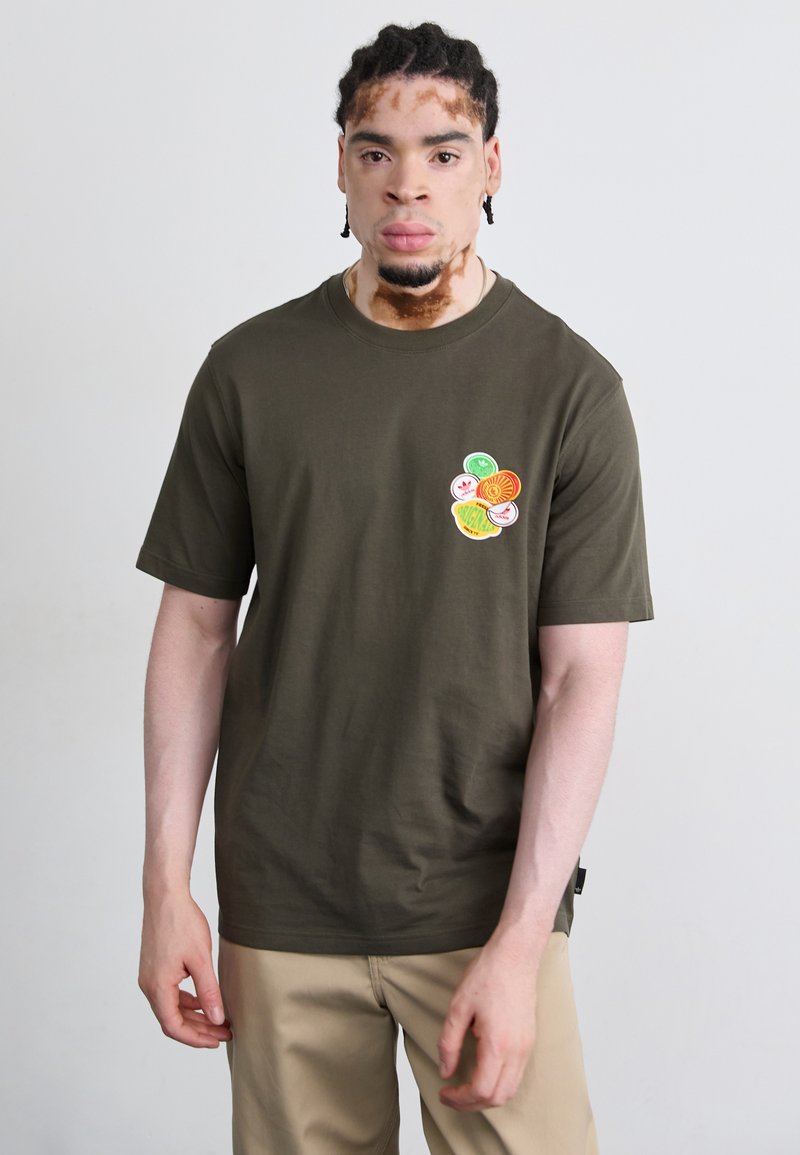 Olivengrøn t-shirt lavet af bomuld, med et farvet grafisk design bestående af cirkulære former på venstre brystområde. Korte ærmer, rund hals.