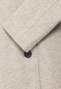Lichtbeige wollen jas manchette met een enkele donkere knop, met textiel met een structuur en nette stikdetails.