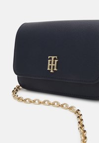 Pochette in pelle texturizzata blu navy con logo monogramma dorato e tracolla in catena dorata su sfondo bianco.