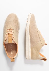 Beige Leinensneaker mit einer strukturierten Oberseite, orangefarbenen Schnürsenkeln und einer gesprenkelten Gummisohle. Lederakzent an der Ferse, minimalistisches Design.