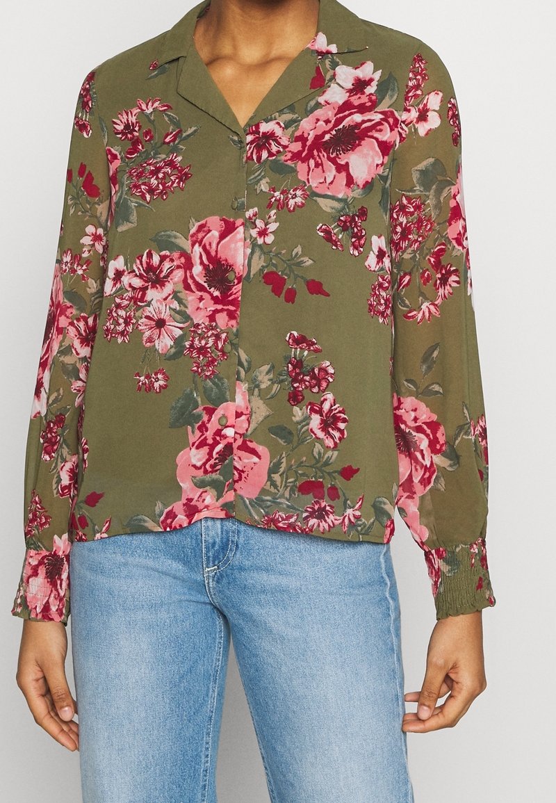 Blommig blus i olivgrön med rosa och vita blommönster, långa ärmar, knappstängning fram och cuffs vid handleden. Lättviktigt tyg.