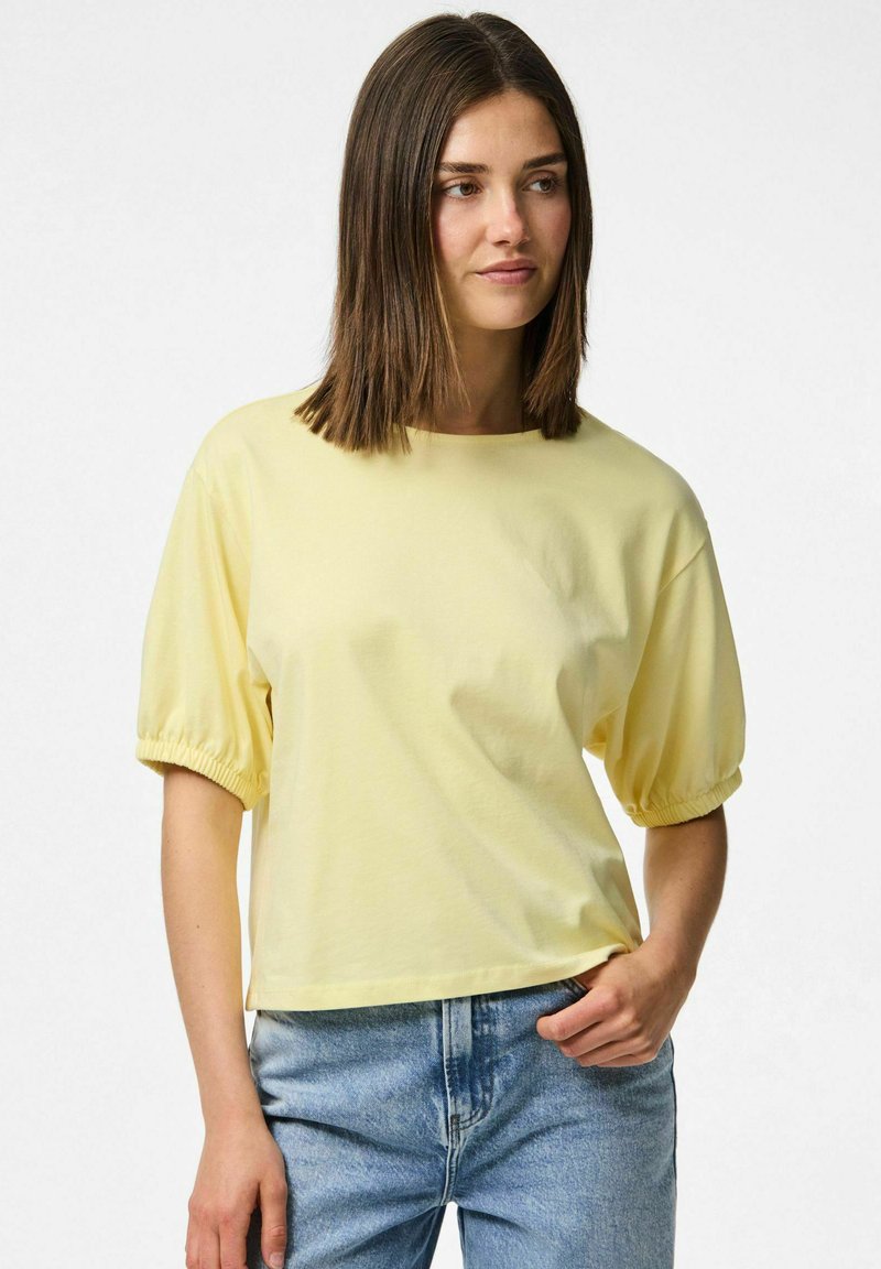 Gul bomulls t-shirt med korta puffärmar, rund halsringning och avslappnad passform, i kombination med ljusblå jeans.