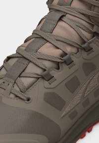 Κοντινό πλάνο ενός πεζοπορικού παπουτσιού σε χρώματα ταουπ και καφέ, με ανώτερο τμήμα από υφασμάτινο πλεκτό, ενισχυμένες οπές για τα κορδόνια, λεπτομερή ραφές και υφασμένο καουτσούκ στη σόλα.