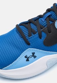 Close-up of blue athletic shoe with black laces, Under Armour logo, and white sole on a white background.