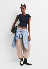 Laivastonsininen crop-top, siniraitainen paita vyötäröllä solmittuna, vaaleanbeige collegehousut ja mustat kengät valkoisilla yksityiskohdilla ja logolla.