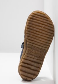 Námořnická bota s gumovou podrážkou, která má texturovanou hnědou spodní část a horizontální drážky pro přilnavost, se zobrazeným názvem značky.