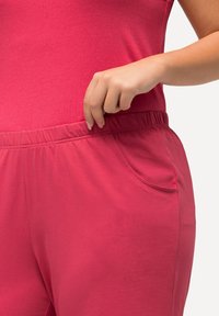 Fuchsiový overal se volným střihem, krátkými rukávy, elastickým pasem a bočními kapsami pro praktičnost. Měkký bavlněný materiál.