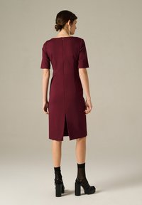 Abito fitted bordeaux con maniche corte, chiusura con zip sul retro e uno spacco all'orlo. Abbinato a scarpe con plateau nere e calzini trasparenti.