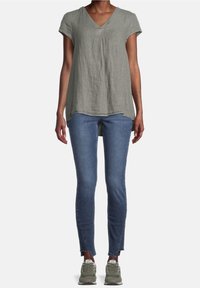 Haut vert clair à manches courtes en V fabriqué en un mélange de lin texturé, associé à un jean bleu ajusté avec des bords bruts et des baskets vert olive.