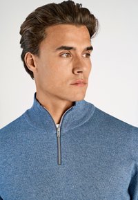 Lichtblauwe zip-up trui met een hoge kraag en ribbelstructuur. Bevat een zilveren rits en een zachte gebreide stof.
