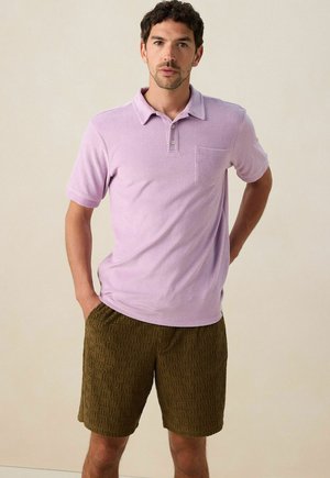 Polo lilas avec col et poche sur la poitrine, associé à un short beige avec un motif géométrique texturé. Manches courtes ; coupe décontractée.