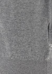 Grau gestrickter Pullover mit ribbeltem Saum und einem kleinen Logoschild an der Seite. Weiche Textur mit subtilen Farbvariationen.