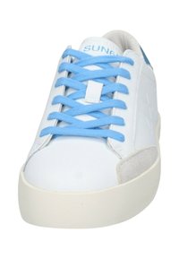 Sneaker bianco con lacci blu, punta arrotondata e suola in gomma chiara. Presenta una tomaia in pelle liscia con un accento in suede.